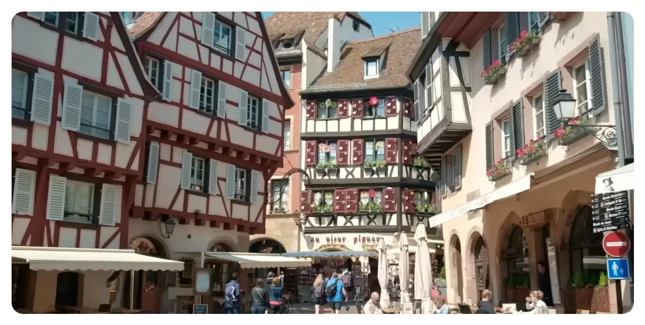 Colmar half-timbered houses lining a square with outdoor café seating on a sunny day
