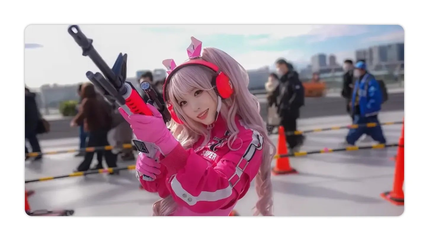 Cosplayer in pink outfit holding a prop weapon with the event area and attendees behind