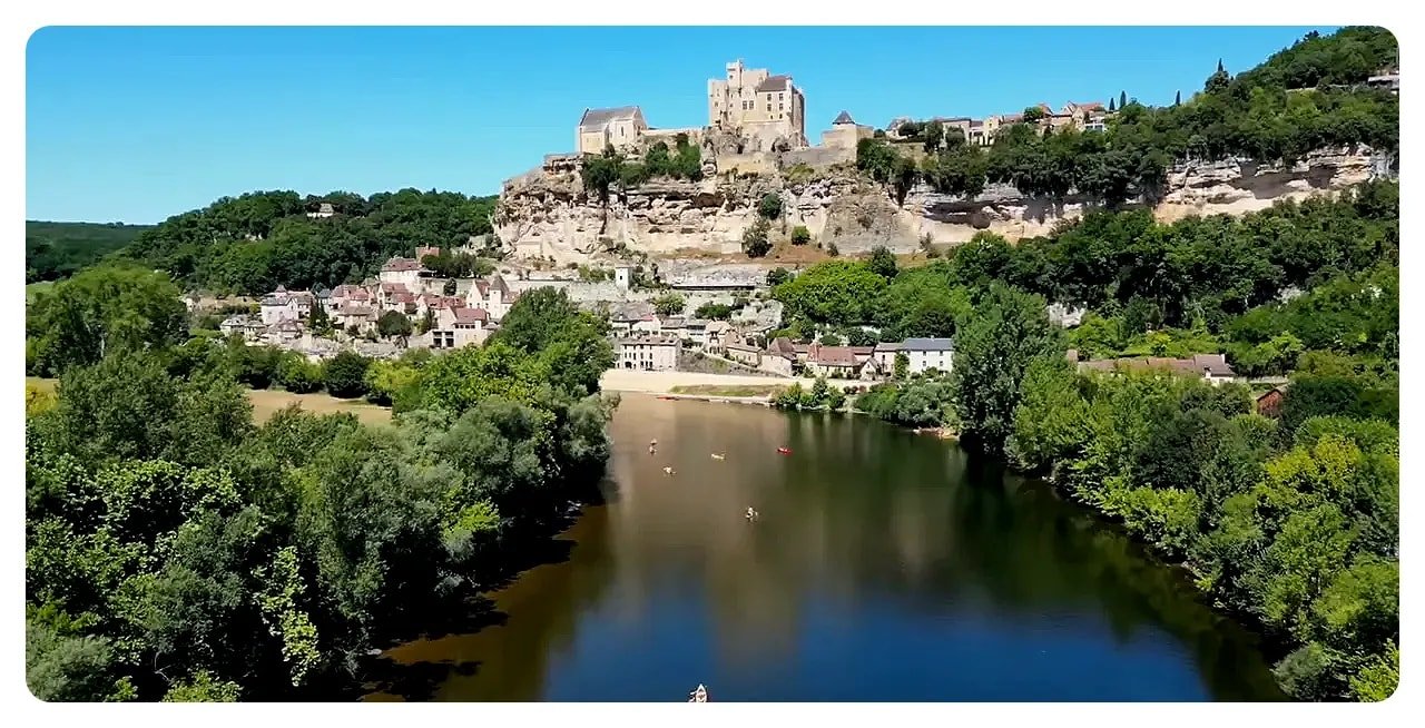 Cliff-top village and château above the Dordogne River with kayakers on the water below