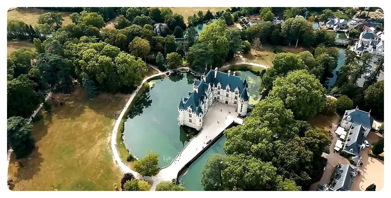 Aerial view of a Loire chateau built over water with a bridge entrance and surrounding trees and gardens