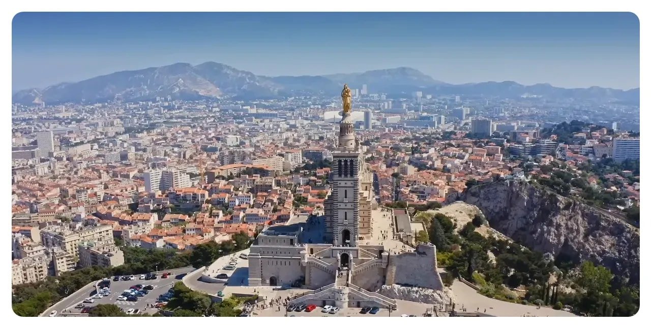 Panoramic aerial of Notre-Dame de la Garde with Marseille's skyline, harbour and distant mountains