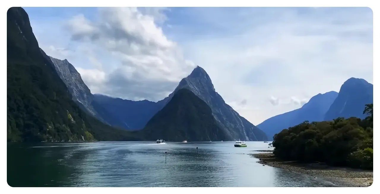Mitre Peak and surrounding fjord at Milford Sound with a few tour boats on calm reflective water