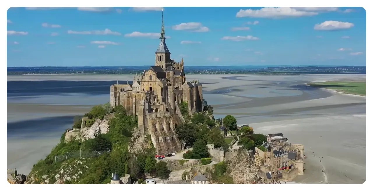 Mont Saint-Michel abbey and village perched on a rocky island with sweeping tidal flats under a blue sky