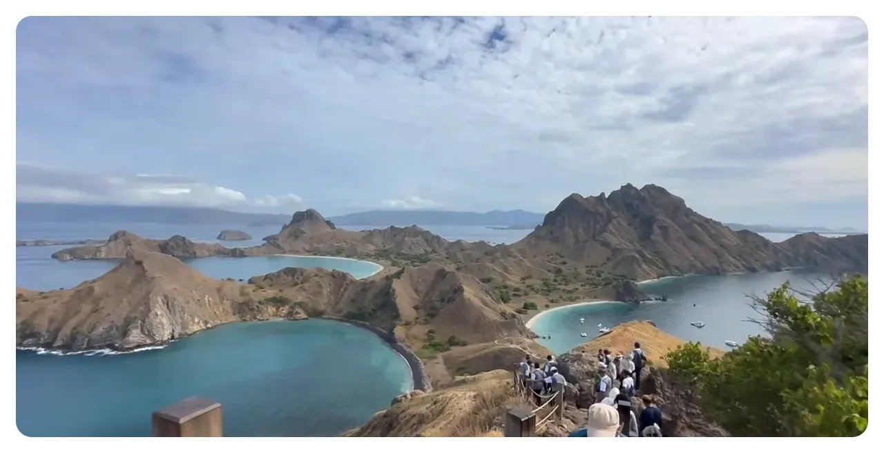 Wide aerial panorama from the Padar ridge showing multiple crescent bays, boats in the water and visitors on the path