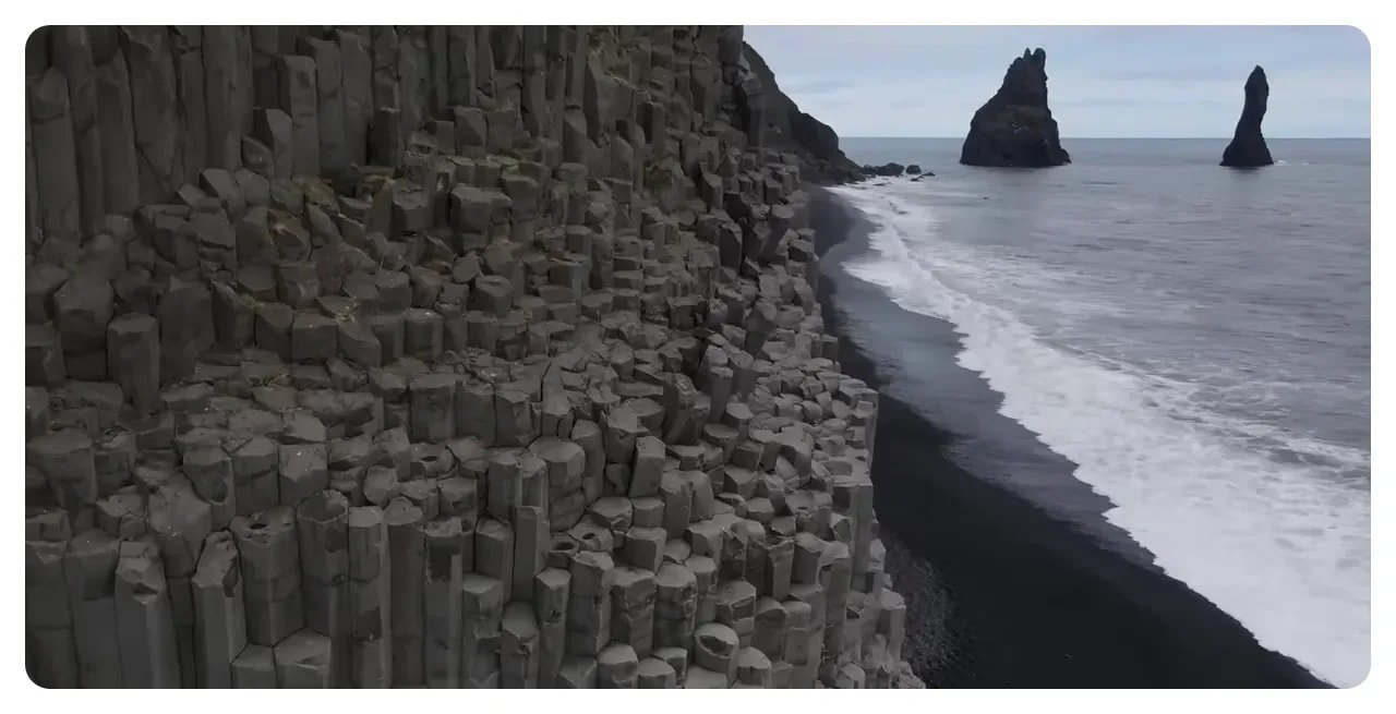 Columnar basalt cliff dropping to a black sand shore with Reynisdrangar sea stacks offshore at Reynisfjara