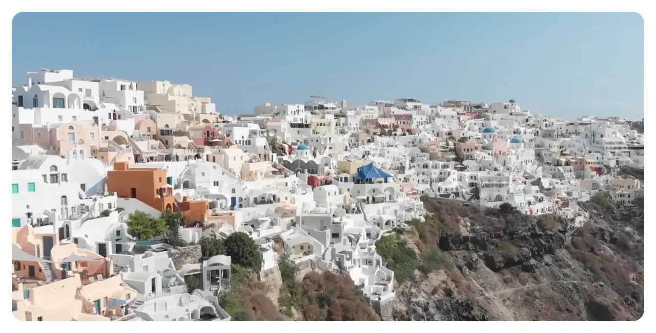Bright aerial panorama of Santorini's whitewashed buildings on the caldera cliff.